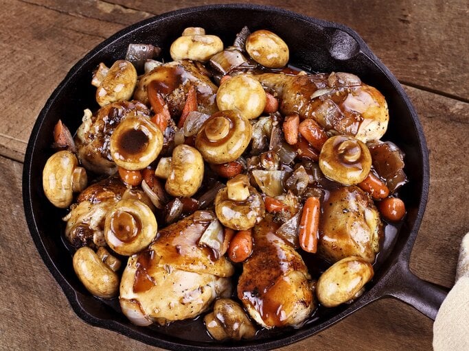 Gusseiserne Pfanne auf Holz gefüllt mit Coq au vin samt Pilze und Fleisch.  | © iStock/ StephanieFrey