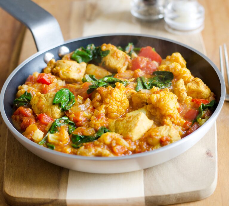 Schmackhaftes Hühnchen-Curry mit Tomaten und Spinat, serviert in einer Pfanne auf einem Holzbrett. | © iStock/LC martinturzak