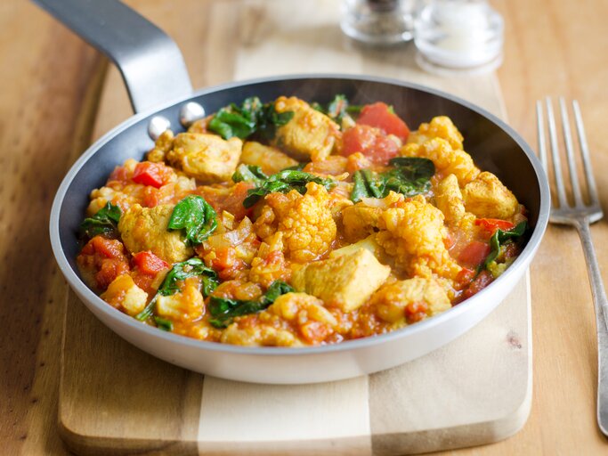 Schmackhaftes Hühnchen-Curry mit Tomaten und Spinat, serviert in einer Pfanne auf einem Holzbrett. | © iStock/LC martinturzak
