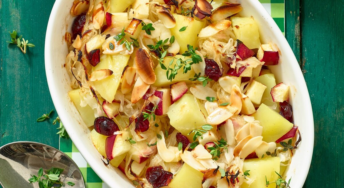 Kartoffel-Sauerkraut-Auflauf in einer ovalen Schüssel von oben fotografiert. Unten auf dem Foto ein Löffel, oben Petersilie.