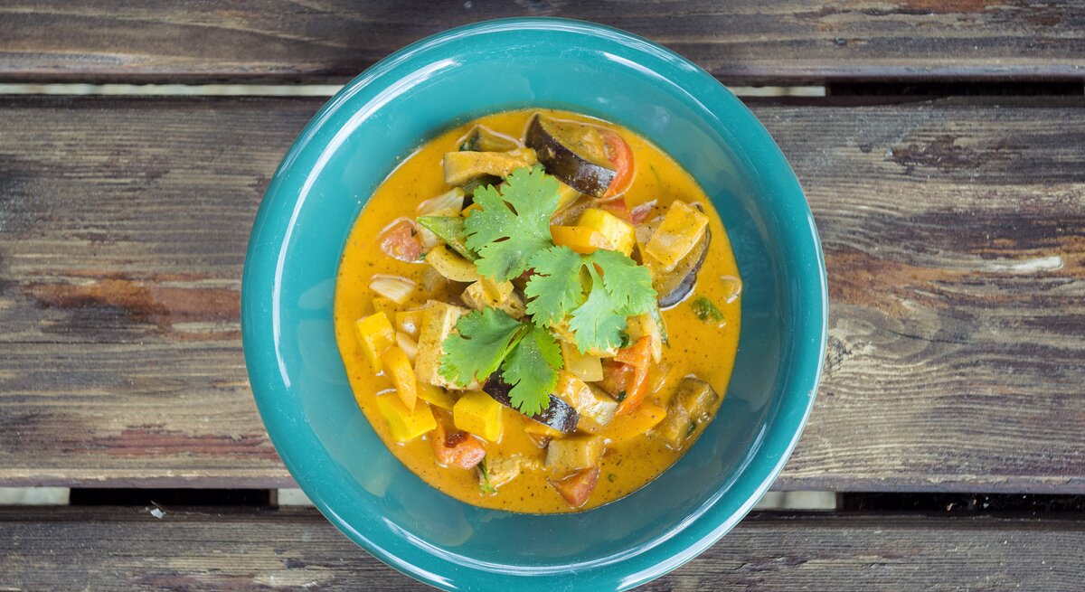 Ein grüner Teller mit würzigem Curry aus Gemüse und Koriander auf einem rustikalen Holztisch.