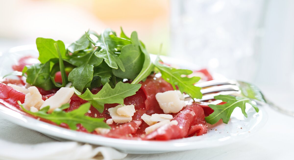 Seitenansicht auf einen weißen Teller belegt mit Rinder-Carpaccio