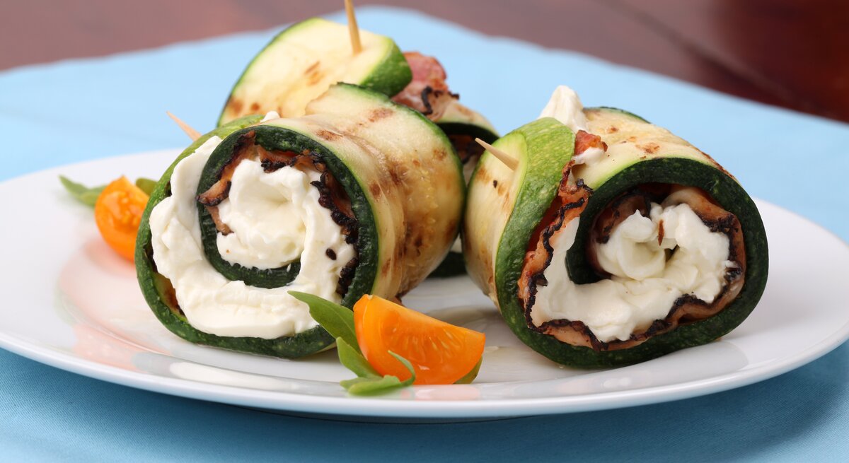 Zucchini-Schinken-Röllchen mit Mozzarella auf weißem Teller. 