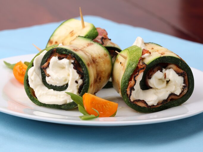 Zucchini-Schinken-Röllchen mit Mozzarella auf weißem Teller.  | © iStock/ IngridHS 