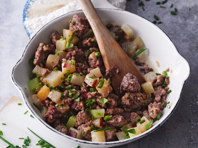 Draufsicht: Eine  weiße Hackfleischpfanne mit Kohlrabi. In dem Essen steckt ein großer Löffel aus Holz. | © StockFood/Gräfe & Unzer Verlag/Kramp + Gölling