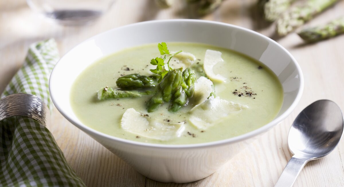 Spargelcremesuppe mit Parmesan in weißer Schale garniert mit Spargelköpfen. 