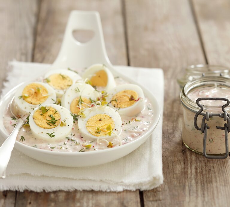 Die gekochten und halbierten Eier in Merrettichsauce auf einem weißen Teller und dunklem Holztisch. | © StockFood / StockFood / Castilho, Rua