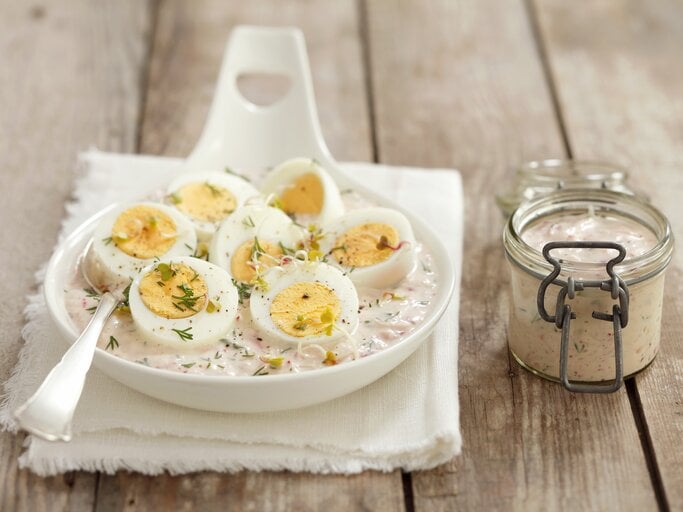 Die gekochten und halbierten Eier in Merrettichsauce auf einem weißen Teller und dunklem Holztisch. | © StockFood / StockFood / Castilho, Rua