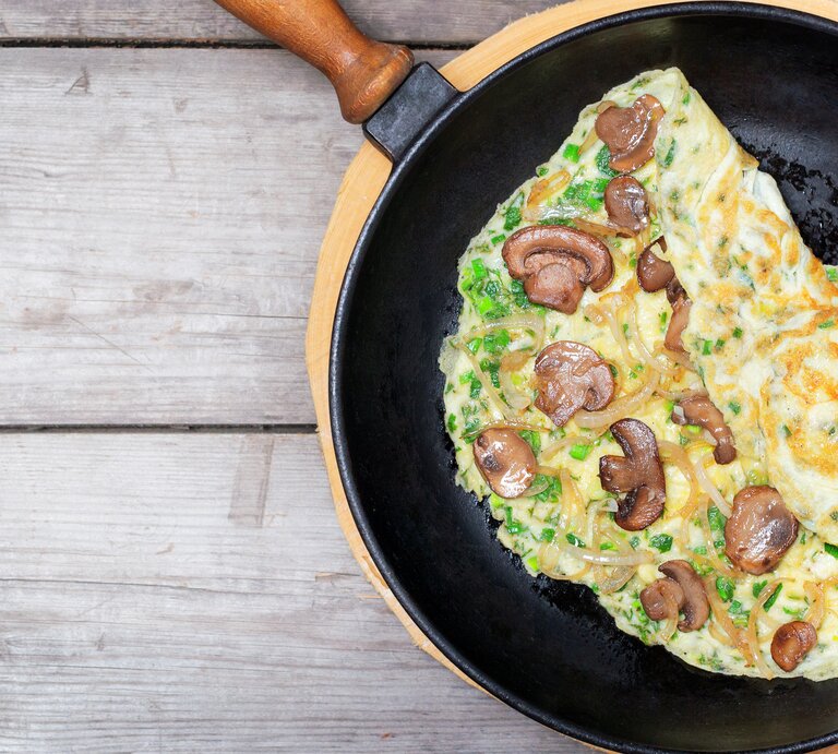 Eine Pfanne mit dem Pilz-Omelette auf einem hellen Holztisch direkt von oben fotografiert. | © iStock/ YSedova