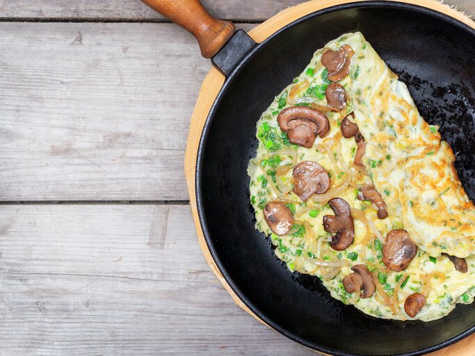 Eine Pfanne mit dem Pilz-Omelette auf einem hellen Holztisch direkt von oben fotografiert. | © iStock/ YSedova