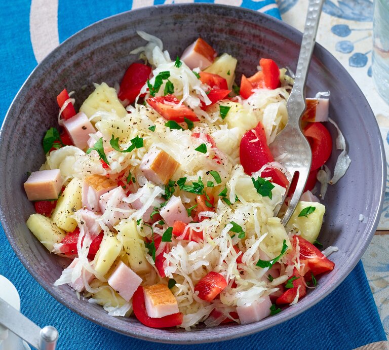 Sauerkrautsalat mit Kasseler in einer Schüssel auf einem blauen Untersetzer. Darunter eine Tischdecke mit blauen Blumen. | © Matthias Liebich