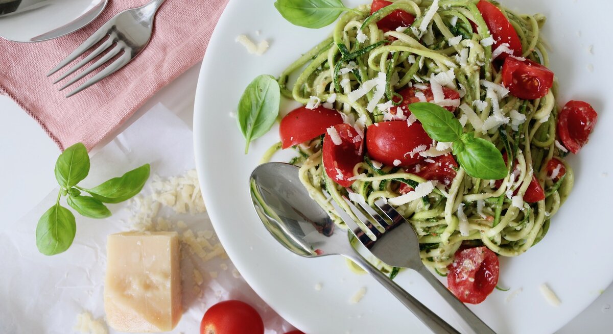 Zucchini Spaghetti mit grünem Pesto, Kirschtomaten und Parmesan auf einem Teller.