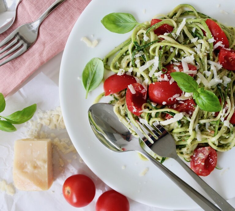 Zucchini Spaghetti mit grünem Pesto, Kirschtomaten und Parmesan auf einem Teller. | © Nadine Hüttenrauch