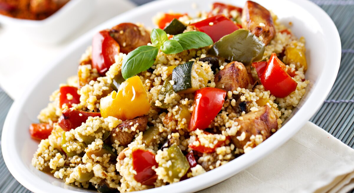 Weißer Teller, darauf Couscous-Salat mit Gemüse und Hähnchen.