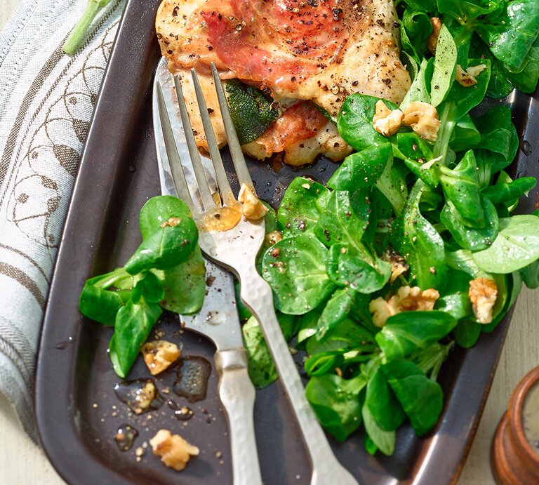 Hähnchenbrustfilet mit Parmaschinken auf Salat auf einem schwarzen Teller. | © Matthias Liebich