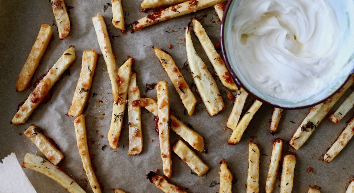 Auf einem Blech liegen Low-Carb-Pommes aus Pastinake. Daneben ist ein weißer Dip in einer Schüssel.
