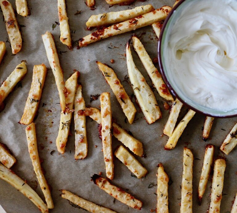 Auf einem Blech liegen Low-Carb-Pommes aus Pastinake. Daneben ist ein weißer Dip in einer Schüssel. | © Nadine Hüttenrauch