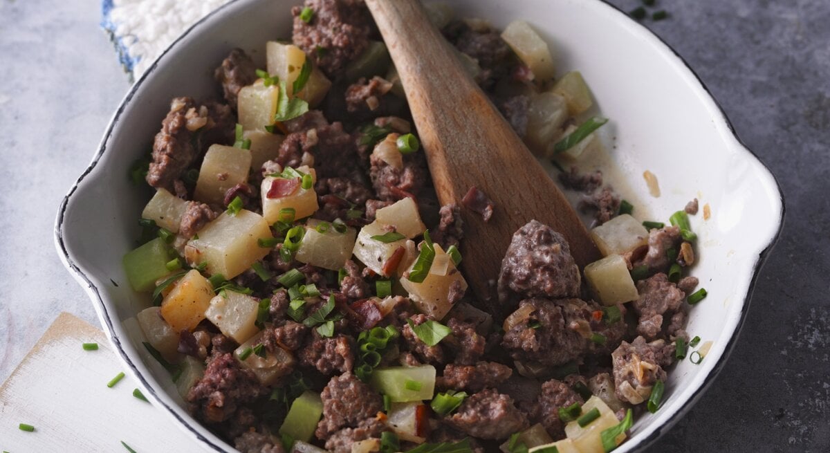 Hackfleischpfanne mit Gemüse und Schinken / runde Schüssel mit Holzlöffel / Draufsicht, schräg