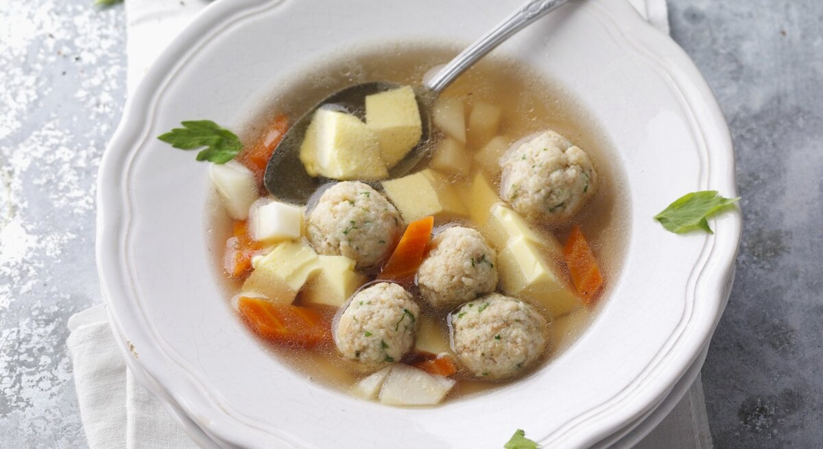 Ein weißer Teller mit der Rindfleischsuppe auf grauem Untergrund direkt von oben fotografiert.