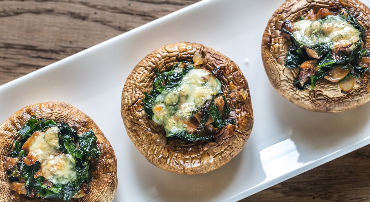 Draufsicht auf drei mit Spinat und Käse gefüllte Champignons. 