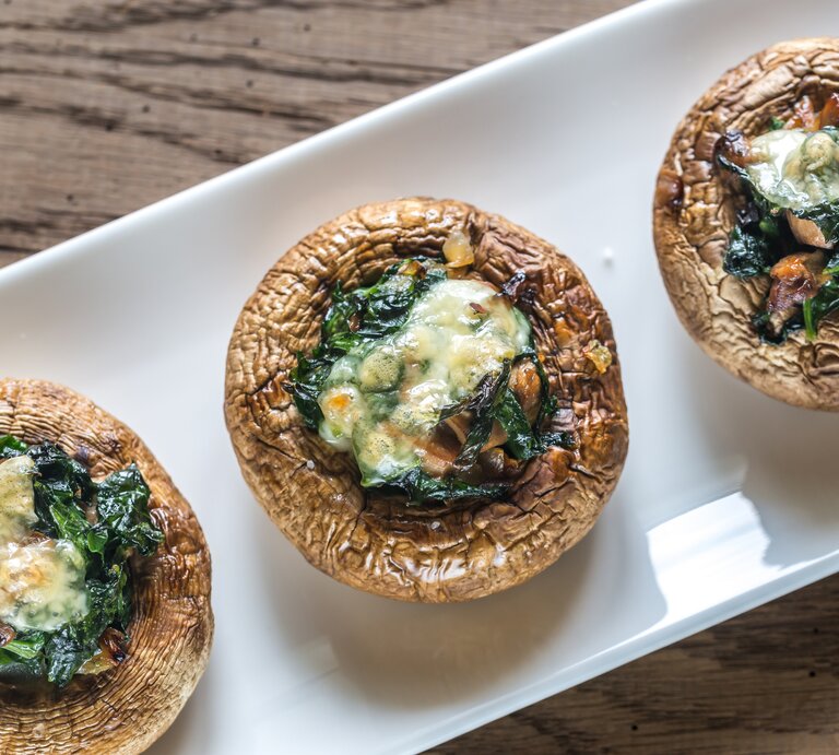 Draufsicht auf drei mit Spinat und Käse gefüllte Champignons.  | © iStock/ AlexPro9500