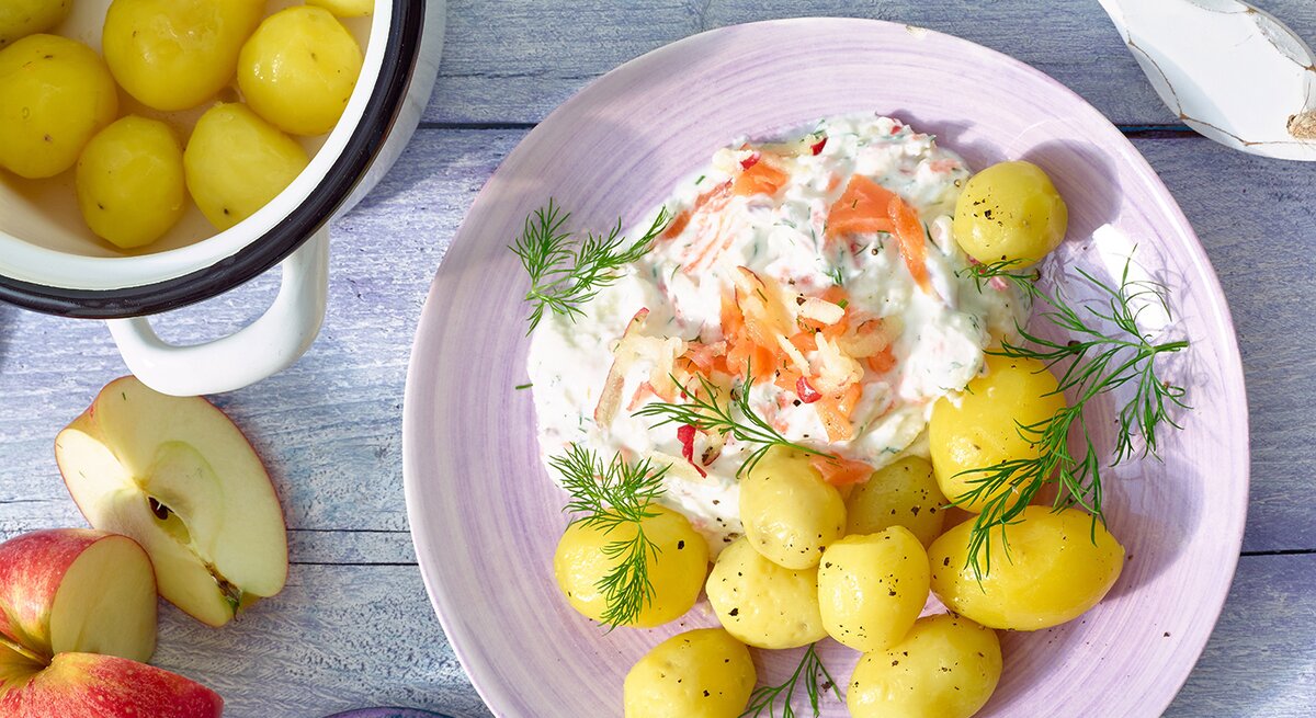 Draufsicht: Auf einem Tisch, ein runder Teller mit gekochten Kartoffeln und einer Quark-Creme mit Lachs.