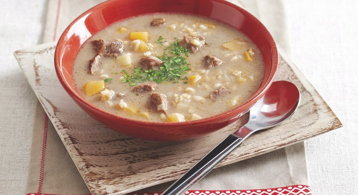 Graupensuppe in rundem Teller / Löffel / Untergrund Holzschlale auf Tisch 