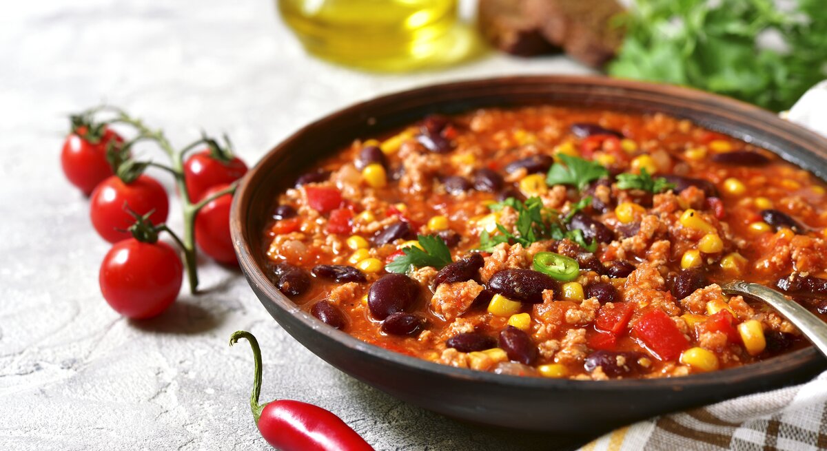 Dunkler Suppenteller gefüllt mit Chili con carne mit Mais und Kidneybohnen vor weißem Hintergrund. 
