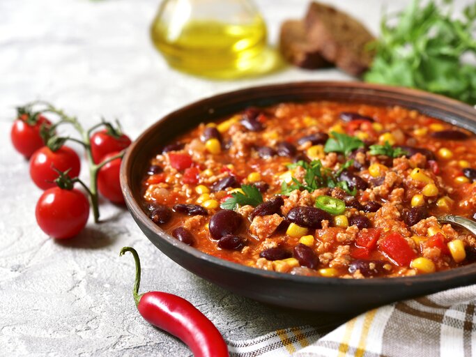 Dunkler Suppenteller gefüllt mit Chili con carne mit Mais und Kidneybohnen vor weißem Hintergrund.  | © iStock/Lilechka75