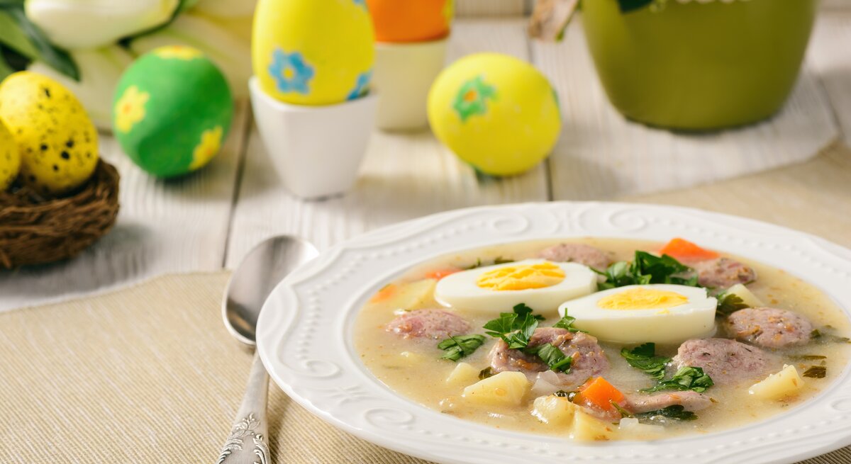 Ein Teller mit der Suppe auf einem hellen Holztisch und Oster-Dekoration. 