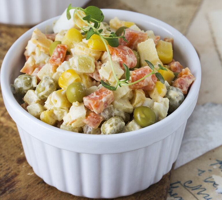 Eine kleine weiße Schale gefüllt mit einem Kartoffelsalat mit Mais, Ei, Erbsen, Karotten und Mayonnaise. | © StockFood/Laniak, Malgorzata