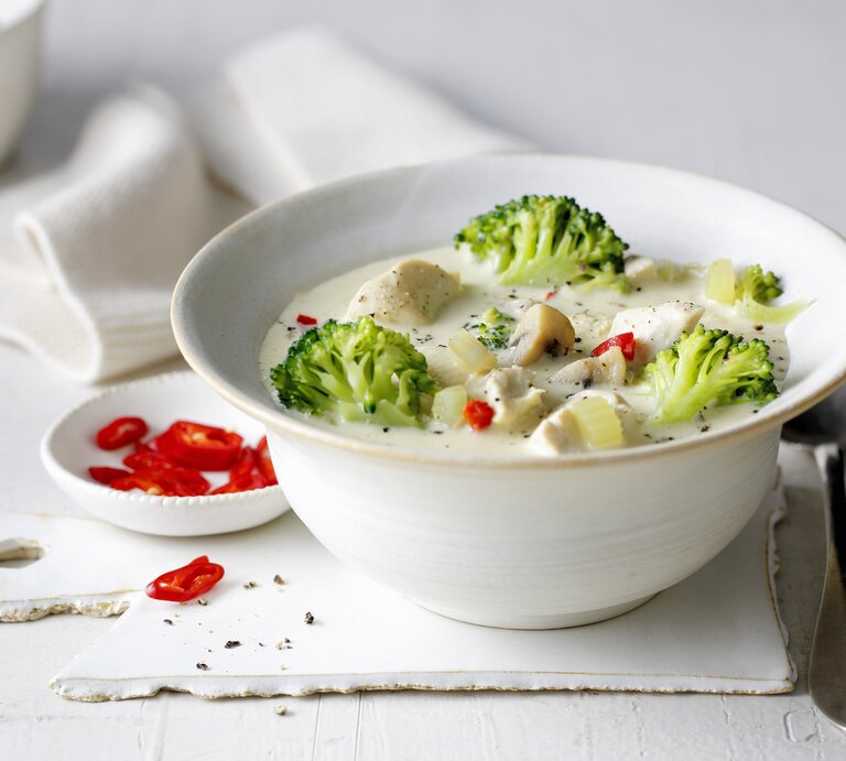 Eine weiße Schale mit der Hähnchen-Brokkoli-Suppe auf einem weißen Tisch von der Seite fotografiert. | © StockFood / Gräfe & Unzer Verlag / mona binner PHOTOGRAPHIE