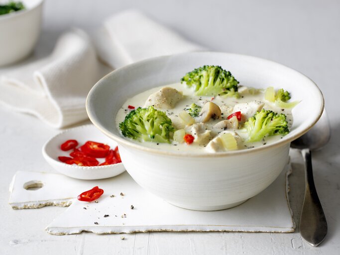 Eine weiße Schale mit der Hähnchen-Brokkoli-Suppe auf einem weißen Tisch von der Seite fotografiert. | © StockFood / Gräfe & Unzer Verlag / mona binner PHOTOGRAPHIE