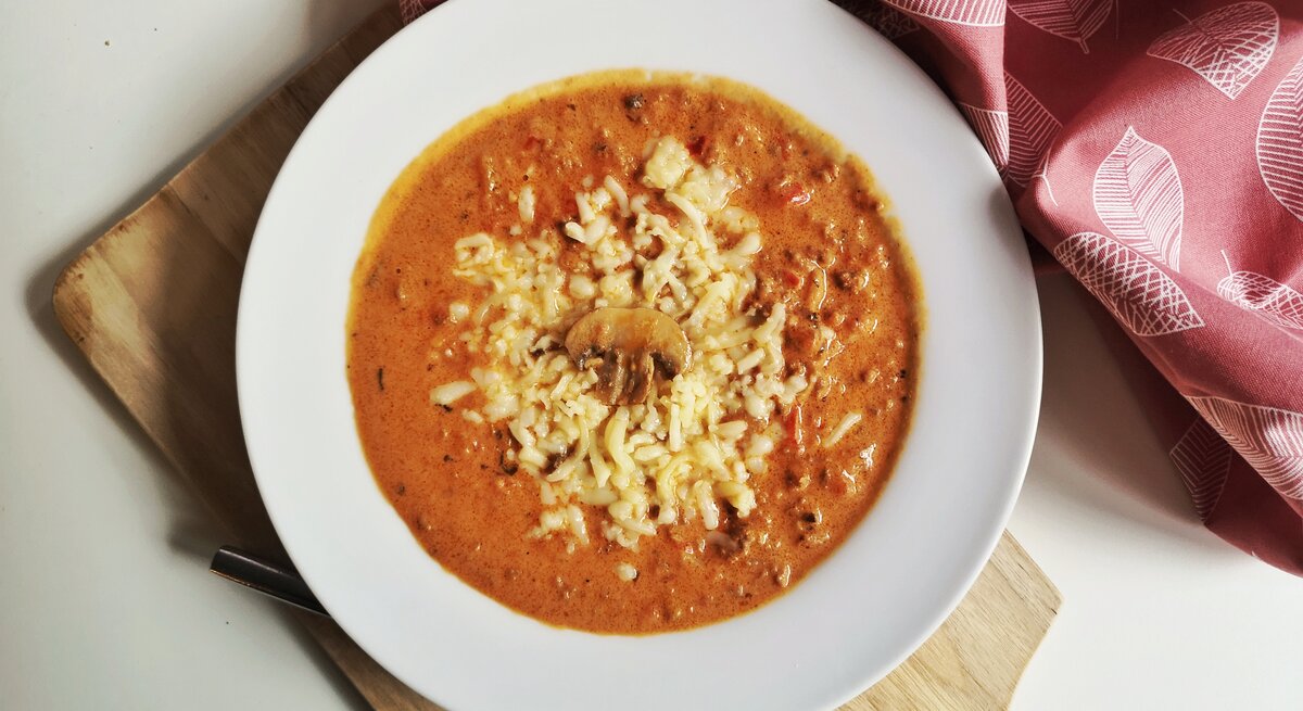 Draufsicht auf einen Teller mit einer tomatigen Pizzasuppe mit Hackfleisch und Pilzen. 