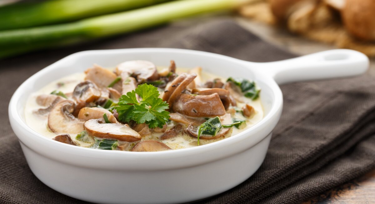Champignons in Sahnesoße in einer kleinen, weißen Pfanne. 