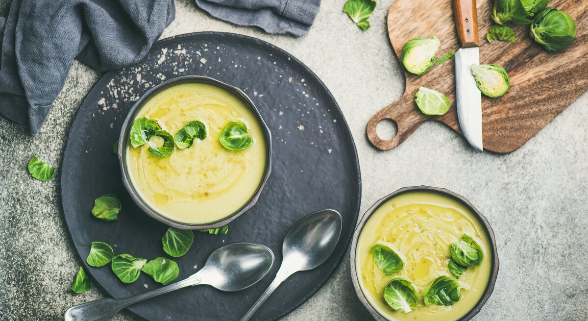Draufsicht auf eine runde Schüssel gefüllt mit einer cremigen Suppe aus Rosenkohl. Das Ganze steht auf einem runden untersetzer. 