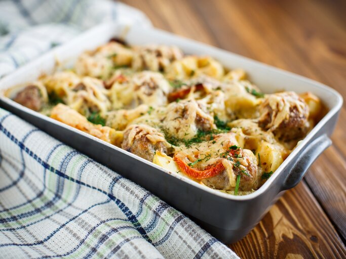 Auflauf mit Kohlrabi und Hackfleisch in einer Auflaufform auf einem Geschirrtuch auf hölzernem Hintergrund.  | © iStock/peredniankina
