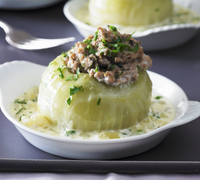Gefüllter Kohlrabi mit Hackfleisch in einem tiefen weißem Teller auf grauem Untergrund. Im Hintergrund ist unscharf eine zweite Portion im Teller zu sehen. | © Stockfood/Walter Cimbal