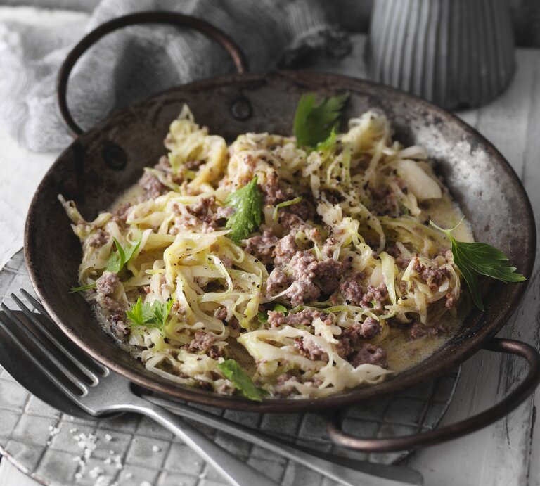 Eine schwarze Pfanne mit dem Gericht auf einem hellgrauen Tisch mit dunkler Dekoration. Alles von schräg oben fotografiert. | © StockFood / Gräfe & Unzer Verlag / Kramp + Gölling