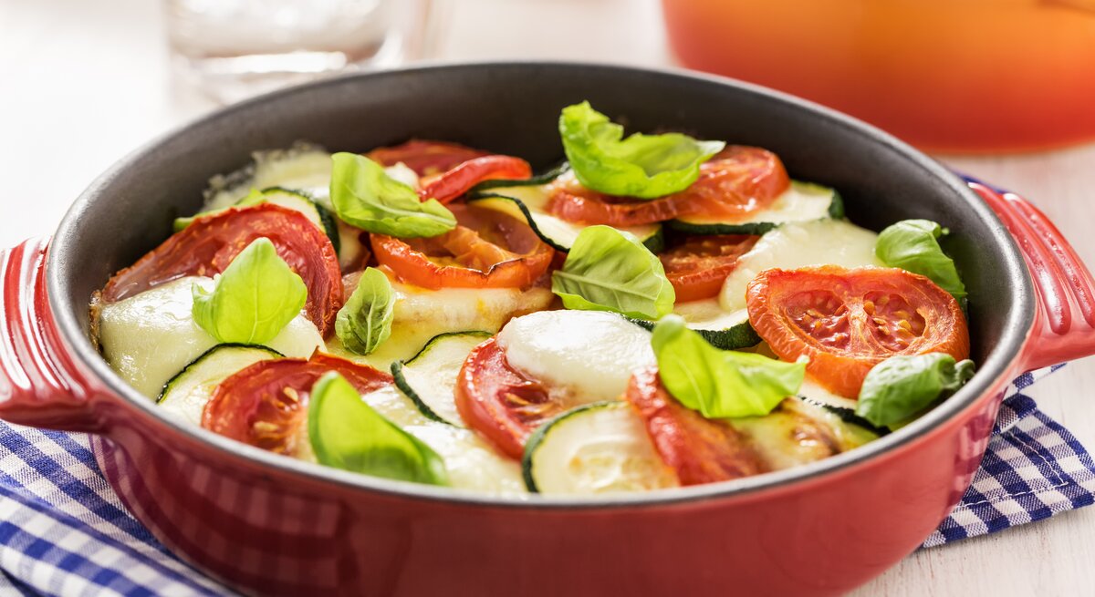 rote, runde Auflaufform gefüllt mit Zucchini, Tomate und Mozzarella.