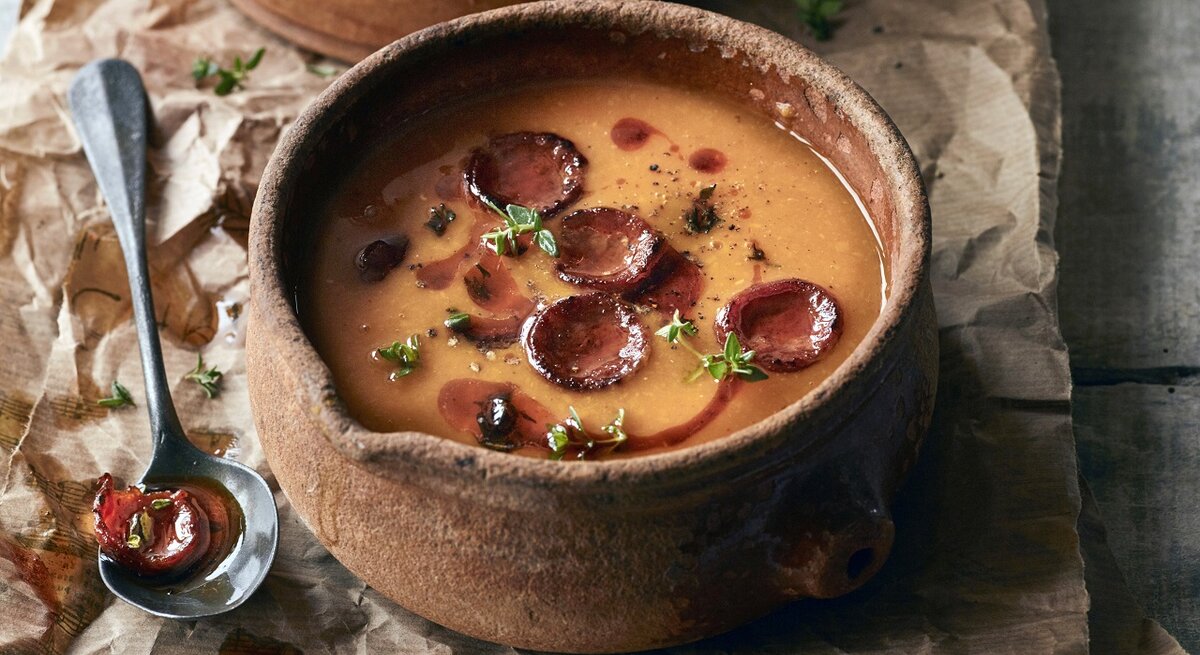 Rustikale Schale mit Kürbissuppe und gebratener Salami. 