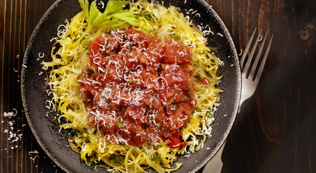 Draufsicht auf einen runden Teller. Darauf angerichtet ist ein gegarter Spaghettikürbis mit Tomatensoße.