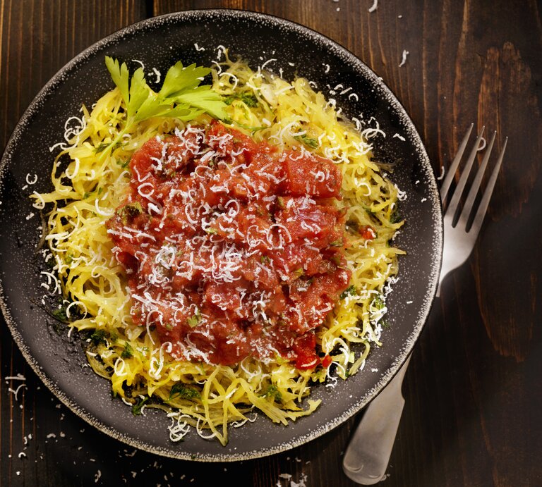 Draufsicht auf einen runden Teller. Darauf angerichtet ist ein gegarter Spaghettikürbis mit Tomatensoße. | © iStock.com/ LauriPatterson