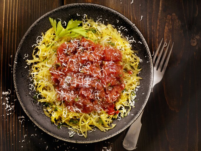 Draufsicht auf einen runden Teller. Darauf angerichtet ist ein gegarter Spaghettikürbis mit Tomatensoße. | © iStock.com/ LauriPatterson