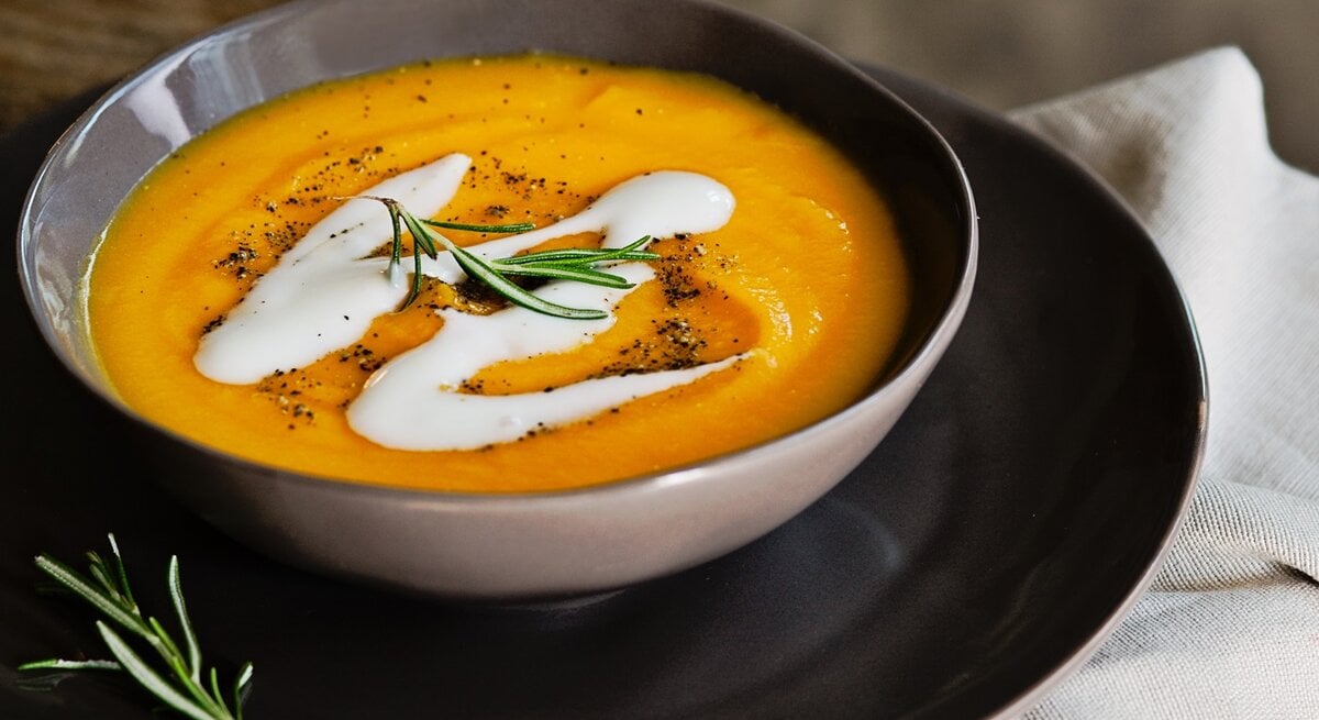 Dunkler Teller mit Kürbissuppe, garniert mit Kokosmilch und Rosmarin. 