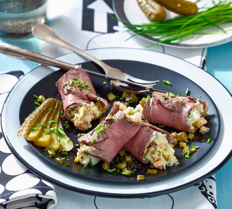 Roastbeef mit Eiersalat auf einem Teller auf einem schwarz-weiß-gemusterten Tischtuch. Hinten auf den Foto ein Teller mit Essiggurken und Schnittlauch. | © Matthias Liebich