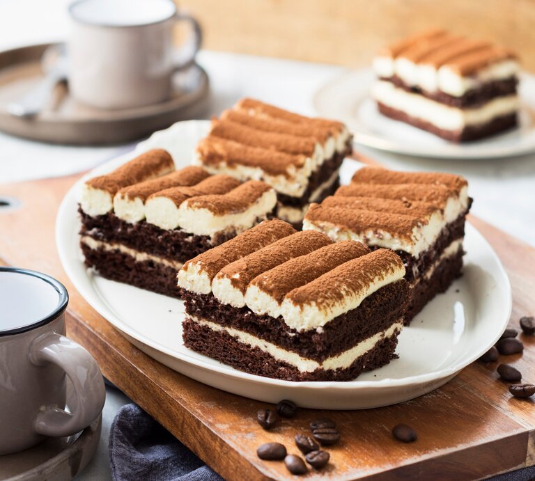 Ein weißer Teller mit drei Stücken der Tiramisu-Torte mit Mascarponecreme auf einem dunklen Holztisch. | © StockFood / ZS Verlag / Speck, Sabrina
