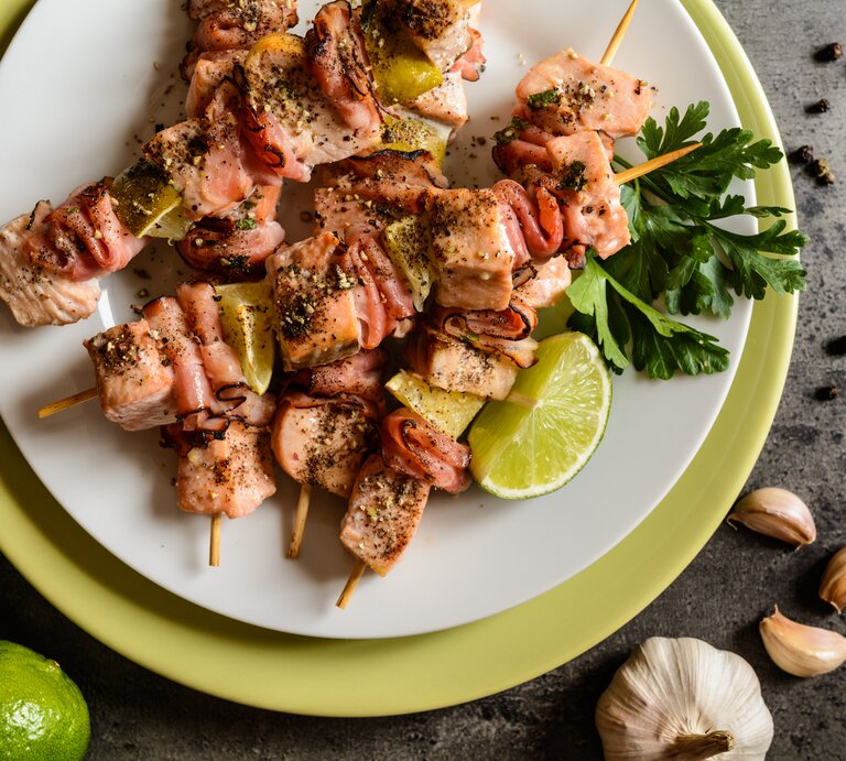 Mehrere Lachsspieße mit Limette auf einem weißen Teller.  | © iStock/ NoirChocolate