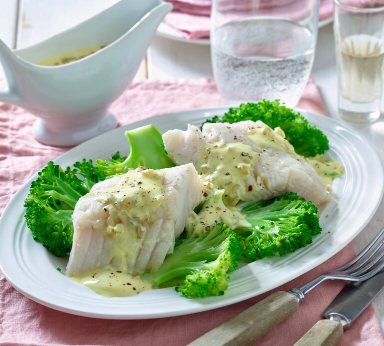 Zanderfilet mit Brokkoli auf einem runden Teller aus Porzellan / Messer und Gabel / ein Behältnis aus Porzellan mit Sauce / Ein Glas mit Sprudelwasser  | © Matthias Liebich