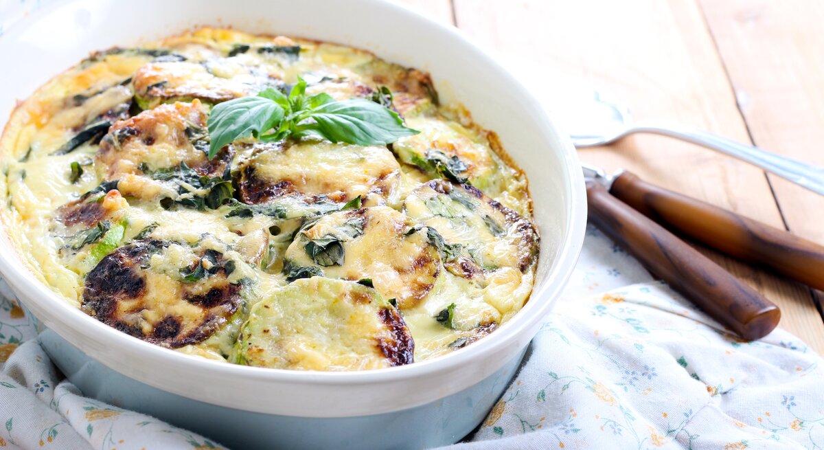 Zucchini-Auflauf mit Käse in blauer Auflaufform. 